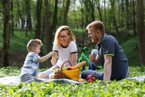 mom-dad-little-boy-taste-apples-sitting-grass-during-picnic-park